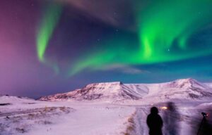 People gazing up at the Northern Lights over a mountain in Iceland