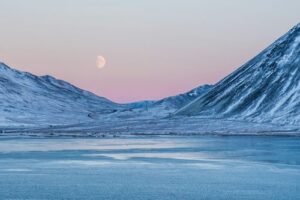 A moon rising on a crimson sky over some snow-covered mountains in Iceland