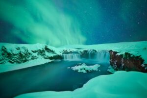 The Northern Lights dancing over Goðafoss waterfall in north Iceland surrounded by snow