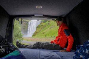 A man camping in a campervan in Iceland during the summer months by Skogafoss waterfall