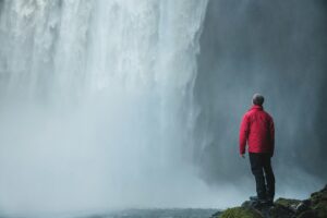 A man standing in front of Skogafoss waterfall as part of a hike in Iceland in summer