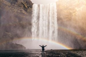 A man celebrating Icelandic National Day under a rainbow at Skogafoss waterfall