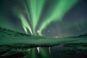 The Northern Lights shining over a snowy mountain top in Iceland