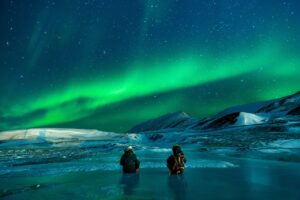 Two people dressed in warm clothes watching the Northern Lights in Iceland