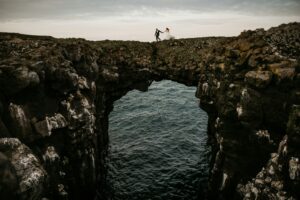 A couple holding hands over Arnarstapi arch in Iceland
