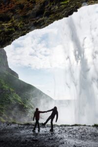 A couple holding hands under Seljalndsfoss waterfall in summer in Iceland