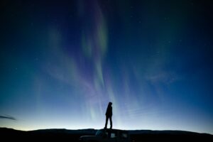 A man stand on top of his car in South Iceland staring up at the Northern Lights